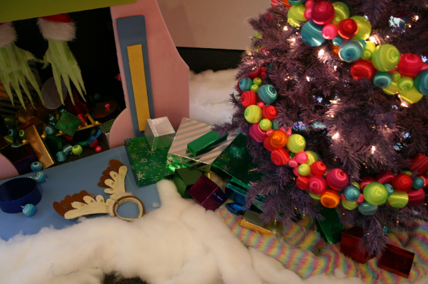 Drinnen, ein geschmückter Weihnachtsbaum rechts, Geschenkboxen und Dekorationsartikel in der Mitte, eine Hütte mit Dekorationen oben links und Baumwolle und Wolle unten.