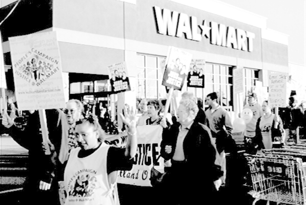 Ein Schwarz-Weiß-Bild von Menschen, die protestieren und Plakate halten, mit einem Einkaufszentrum im Hintergrund.