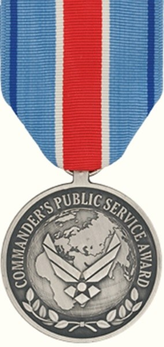 Silberne Medaille mit rot-weiß-blauem Band, beschriftet mit 'Commander's Public Service Award' auf weißem Hintergrund.