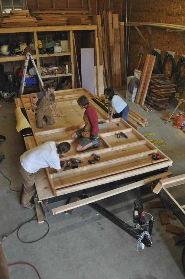 Eine Schreinerwerkstatt mit mehreren Personen bei der Arbeit, umgeben von Werkzeugen und Materialien.