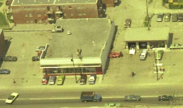 Eine Luftaufnahme einer Stadt mit zahlreichen Autos um Gebäude herum und einigen Autos auf der Straße.