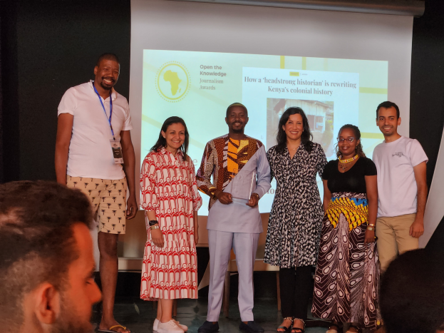 Eine Gruppe von Menschen auf einer Bühne, die lächeln und posieren, vor einem Publikum und einem Bildschirm im Hintergrund, der 'Open the Knowledge Journalism Awards 2019' anzeigt.