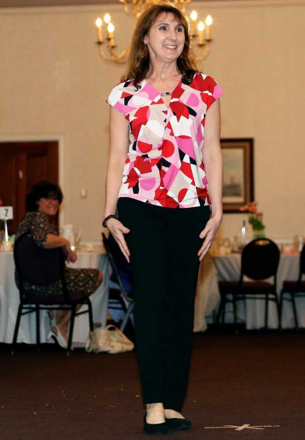 Eine Frau vor einem Bild an der Wand stehend, die lächelt, mit einer anderen Frau auf einem Stuhl neben einem Tisch mit einer Blumenvase.