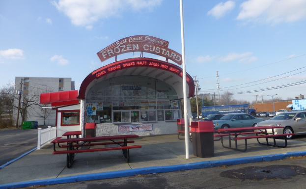 Eine Szene mit Autos, Polen, Gebäuden, Bänken, einem Schuppen mit einer Tafel und Plakaten auf dem Schuppen.
