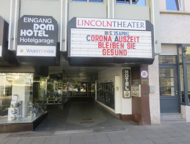 Das Lincoln Theater in Berlin, Deutschland, mit Glasfenstern und -türen und einer Texttafel außen sowie einer belebten Stadtlandschaft durch den Eingang sichtbar.