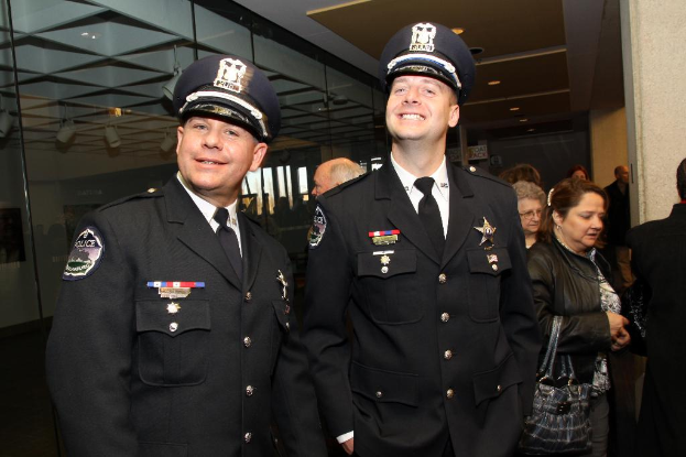 Zwei strahlende Beamte im Vordergrund, mit Menschen in der Mitte, Glasfenstern links, Lampen und Decke oben und Säulen und Menschen rechts.
