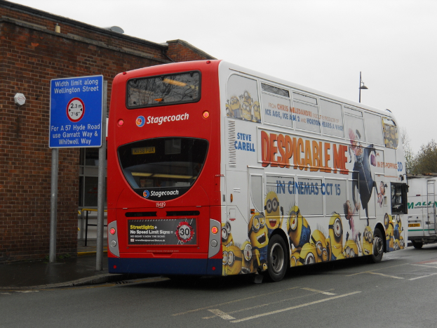 Ein weißer und roter Bus steht auf einer Straße mit einer roten Backsteinmauer und einem blauen Warnschild im Hintergrund.