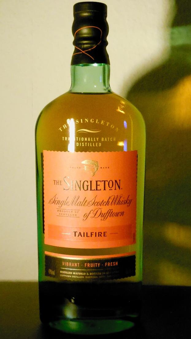 Eine tiefe bernsteinfarbene Flasche Singleton of Dufftown Tailfire Single Malt Scotch Whisky mit einem schwarzen Etikett, das eine schlichte Schrift und ein Wappen mit einem Löwen und einem Schloss zeigt.