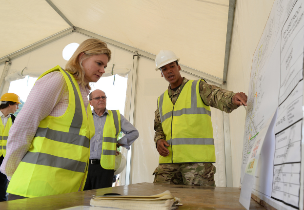 Eine Gruppe von Menschen, einige mit Helmen, versammelte sich um einen Tisch mit Papieren und einem Buch, in einem Zelt.