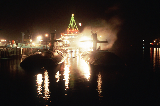 Zwei U-Boote liegen nachts im Wasser mit einem beleuchteten Weihnachtsbaum im Hintergrund.