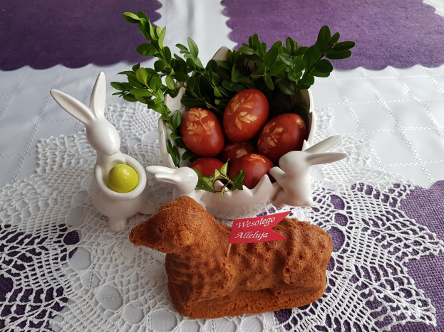 Ein mit einer Decke drapierter Tisch trägt eine Schüssel mit bunten Ostereiern und Osterhasenfiguren darauf.