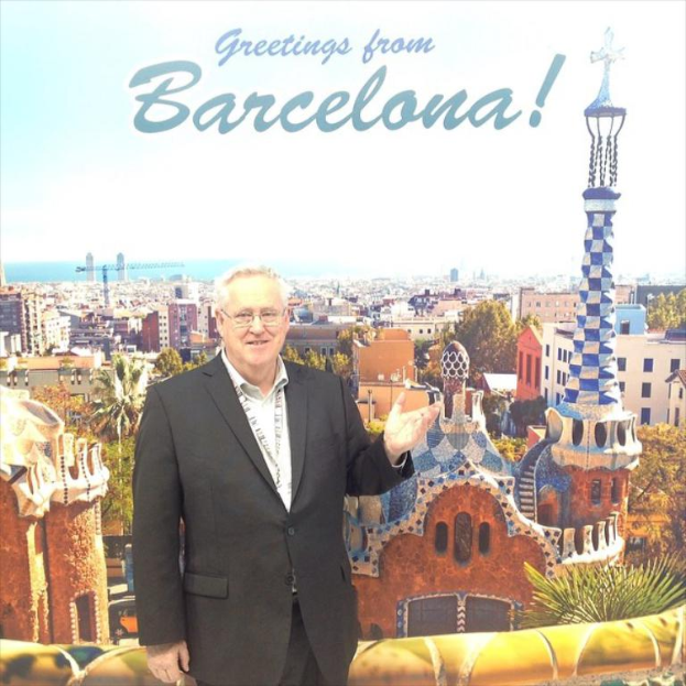 Ein Mann steht vor einem Plakat mit zahlreichen Gebäuden und Türmen, über dem Plakat steht ein Grußtext.