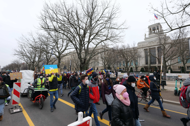 Eine große Gruppe von Menschen nimmt an einer Protestkundgebung in Washington, D.C. am 21. Januar 2020 teil und marschiert eine Straße entlang mit Plakaten, Bannern und Fahrrädern vorbei an einem Gebäude mit Schildern, Bäumen und einem klaren blauen Himmel.