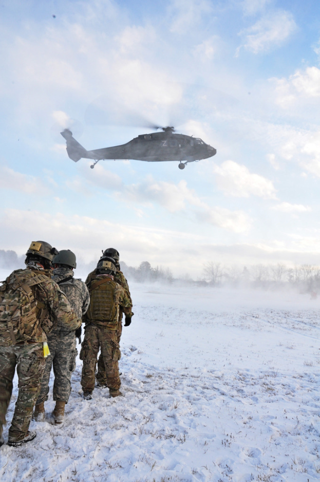 Eine verschneite Landschaft mit Bäumen auf beiden Seiten, vier Männer in Helmen und Taschen auf der linken Seite und ein Flugzeug, das durch die bewölkte Himmel fliegt.