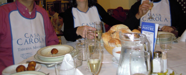 Menschen sitzen an Tischen mit Tellern, Besteck, Gläsern, Brotkörben und einer Werbung.