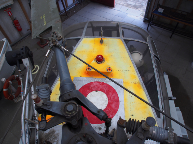 Ein Hubschrauber befindet sich auf dem Boden eines Gebäudes und wird gewartet, mit einem Feuerlöscher auf der linken Seite und einer Bank auf der rechten Seite.