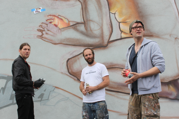 Menschen stehen und halten Farbsprühdosen vor einer Wand mit Graffiti.