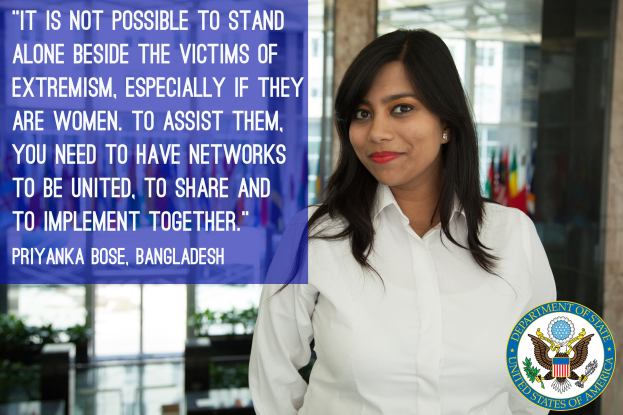 Eine Frau in einem weißen Hemd steht vor einem Gebäude mit einer Aussage über Einheit gegen Extremismus und einem Logo in der rechten unteren Ecke.