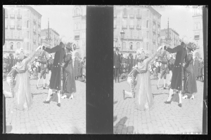 Ein Schwarz-Weiß-Foto einer Gruppe von Menschen, die auf der Straße tanzen, während sie Kostüme tragen und von Gebäuden, Straßenlaternen und einem klaren Himmel umgeben sind.
