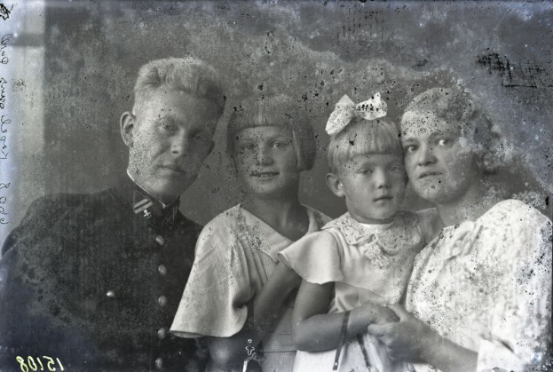 Ein Schwarz-Weiß-Vintage-Foto eines Mannes und einer Frau, die nebeneinander stehen, wobei die Frau ein Kind hält, vor einem unscharfen Hintergrund.
