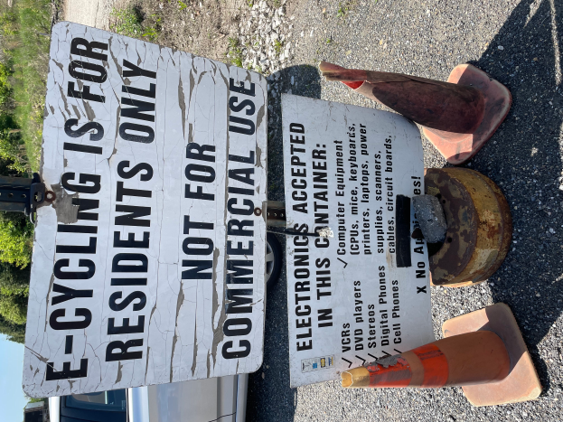 Ein Schild mit der Aufschrift "E-Biking ist nur für Anwohner" steht an der Seite einer Straße, umgeben von Verkehrskegeln und anderen Gegenständen, mit einem Fahrzeug, Bäumen und einem klaren blauen Himmel im Hintergrund.