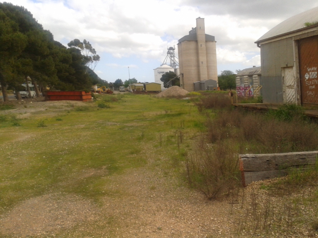 Häuser, Bäume und fabrikähnliche Gebäude auf der linken Seite, mit Bäumen, Fahrzeugen und anderen Gegenständen auf der rechten Seite.
