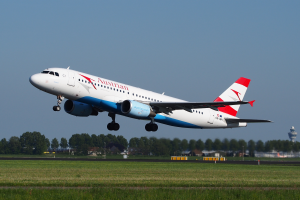 Ein Airbus A320-200 der Austrian Airlines startet am Frankfurter Flughafen, mit grünem Gras, Bäumen, Gebäuden und einem Tower im Hintergrund und dem Himmel oben.