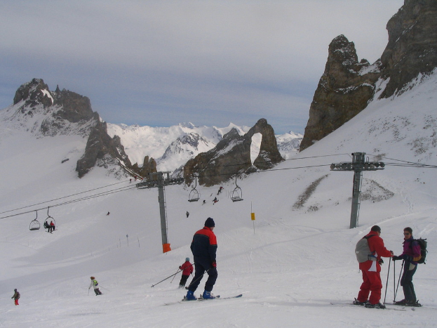 Menschen in Pullovern fahren mit Skiern auf dem Eis und einer Seilbahn im Hintergrund.