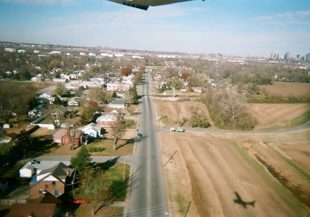Eine Vogelperspektive einer Stadt mit Bäumen und kleinen Hütten im Vordergrund, einer kleinen Straße in der Mitte und vielen Bäumen im Hintergrund.