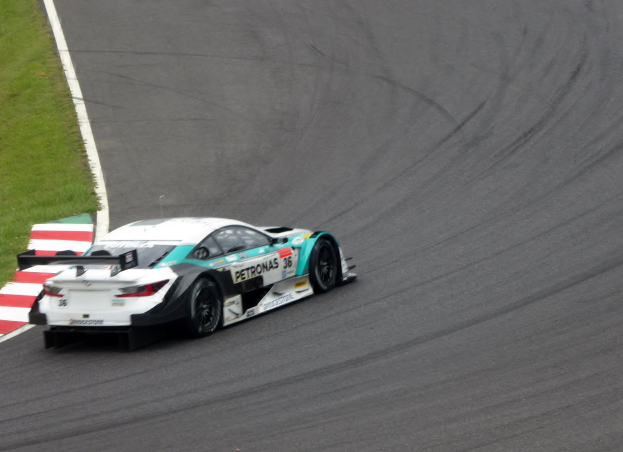 Ein Mercedes-AMG GT3-Rennwagen auf einer Rennstrecke mit Text auf der Karosserie und Gras links daneben.