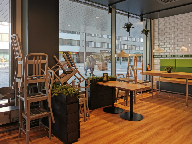 Ein Berliner Restaurant mit Holztischen und -stühlen in der Nähe eines großen Fensters, das eine Straßenszene mit Fußgängern, Gebäuden und städtischen Elementen zeigt.