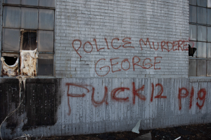 Ein Gebäude mit der Graffiti-Beschriftung "Polizei M"ordet George Fuck 12 P19" an der Seite, das Fenster und verschiedene Gegenstände vor ihm zeigt.