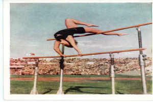 Eine Frau führt einen Hochsprung an parallelen Stangen in einem Stadion mit Zuschauern unter einem klaren blauen Himmel durch.