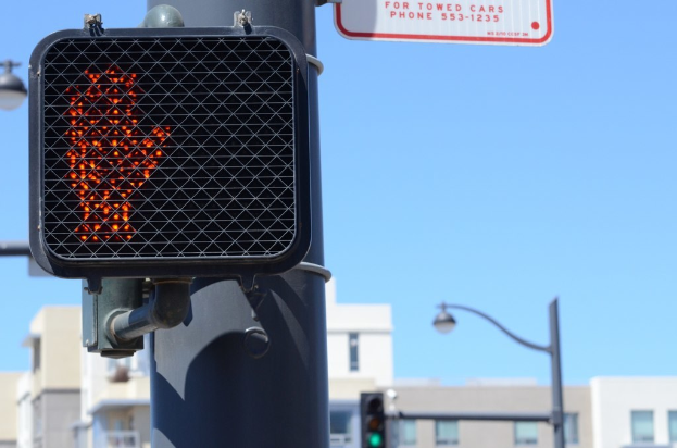 Eine Stadtstraßenszene mit Verkehrspfölen, Ampeln, Straßenpfölen, Straßenlaternen, Gebäuden und einem klaren Himmel.