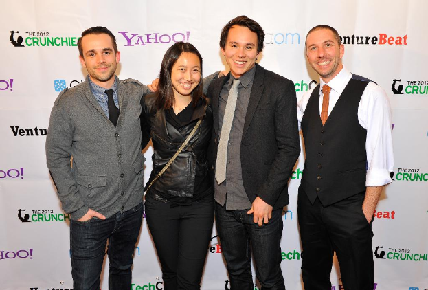 Eine Gruppe von strahlenden Individuen, die vor der Kamera posieren, mit einem Sponsorenbanner im Hintergrund.