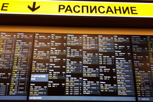 Ein Abflugtafel mit Text und Zahlen, über der ein gelbes Schild hängt, das Fluginformationen anzeigt.