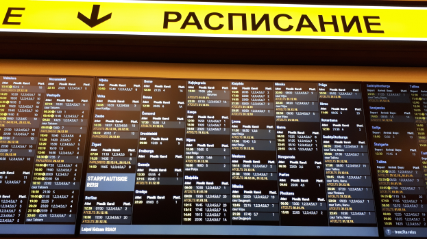 Ein Abflugtafel mit Text und Zahlen, über der ein gelbes Schild hängt, das Fluginformationen anzeigt.
