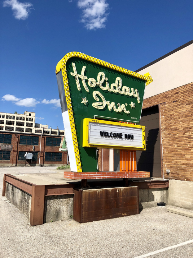Holiday Inn-Schriftzug an einem Gebäude mit einem Textschild davor, bewölktem Himmel und sichtbaren Fenstern im Gebäude.
