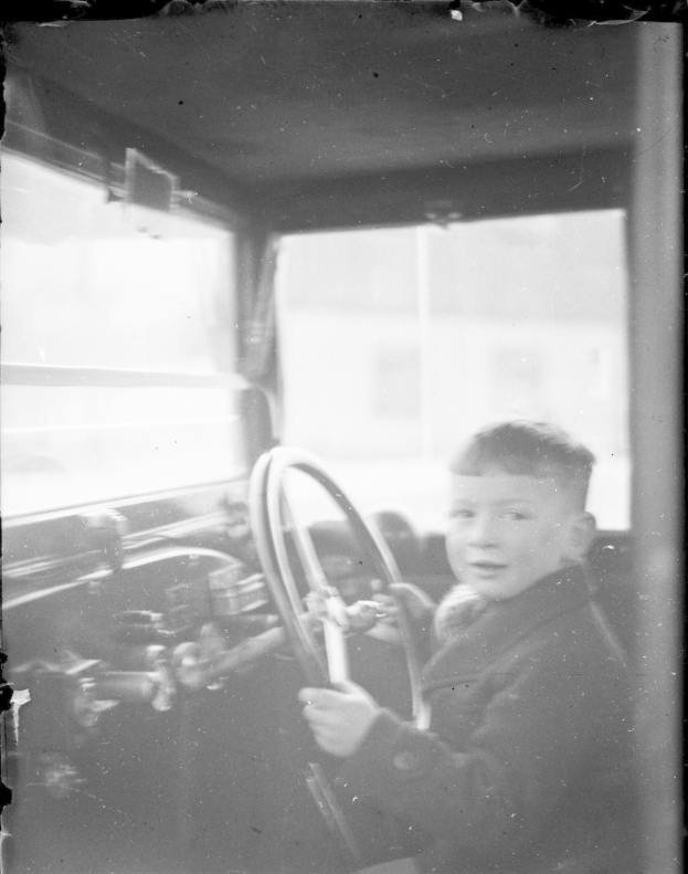 Ein junger Junge in Schwarz-Weiß sitzt im Fahrersitz eines Autos und hält das Lenkrad mit konzentrierter Miene.
