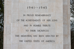 Ein Denkmal mit einer Tafel, auf der "In stolzem Gedenken an die Taten ihrer Söhne und in Demut zu ihrem Opfer" steht, vor einem Hintergrund aus Bäumen und einem klaren blauen Himmel.