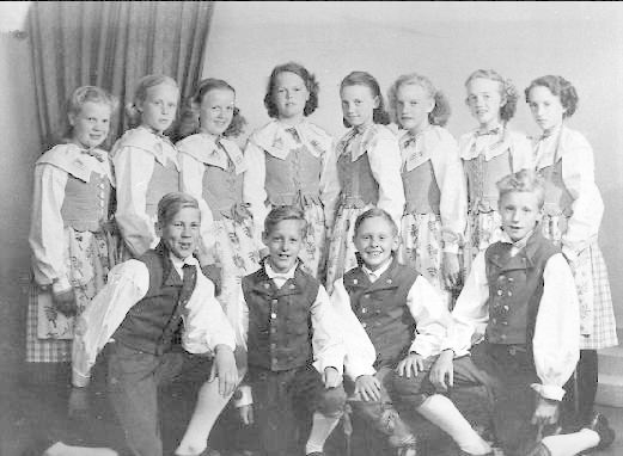 Schwarzes und weißes Foto von Kindern, die vor einer Gardinenwand mit dem Text "1930er Kinder-Schule" posieren.