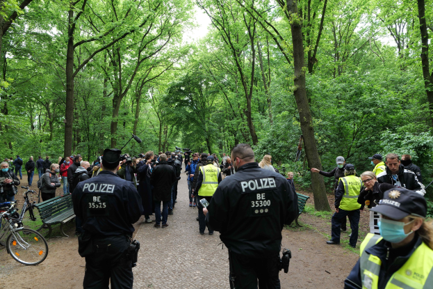 Polizeibeamte vor einer Menschenmenge bei einer Outdoor-Veranstaltung mit Fahrrädern und einer Bank im Vordergrund.
