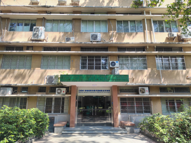 Ein großes Krankenhausgebäude mit zahlreichen Fenstern und Klimaanlagen, umgeben von Grünflächen, mit einer Straße, die darauf zuführt.