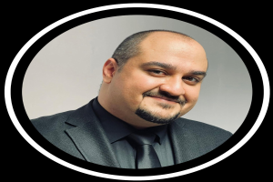 Ein Mann in Anzug und Krawatte mit einem Lächeln vor einem schwarzen Hintergrund, als Anwalt in New York City bezeichnet.