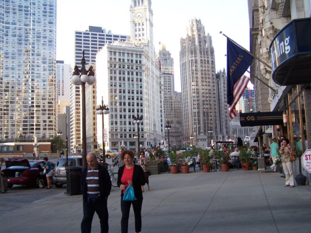 Eine belebte Straßen Szene mit Menschen, Blumentöpfen, Autos, Straßenlaternen, Gebäuden, Geschäften und Fahnen im Hintergrund.