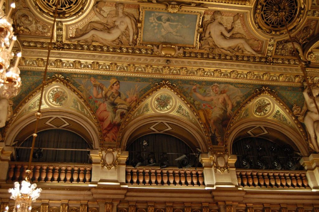 Eine Wand mit Skulpturen, ein Gemälde und ein Rahmen, mit Kronleuchtern und Lampen, eine Balkontür mit Vorhängen.