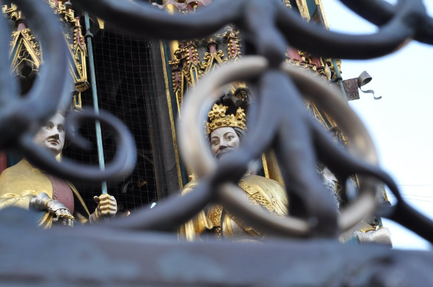 Ein eisernes Geländer mit einer Kirche im Hintergrund, das zwei goldverzierte Statuen und goldene Skulpturen und Verzierungen auf der Kirche zeigt.