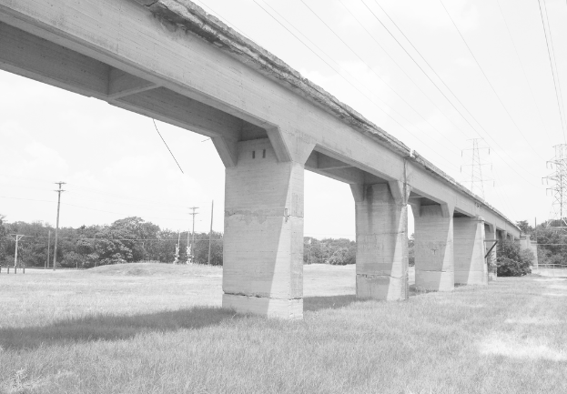 Eine Betonbrücke auf einer grünen Wiese mit einem großen elektrischen Mast und Kabeln darüber, umgeben von Bäumen und zusätzlichen elektrischen Masten im Hintergrund.
