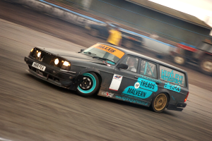 Ein Auto fährt mit einem Fahrer auf einer Rennstrecke, umgeben von anderen Fahrzeugen, mit einem unscharfen Hintergrund, der hohe Geschwindigkeit andeutet.