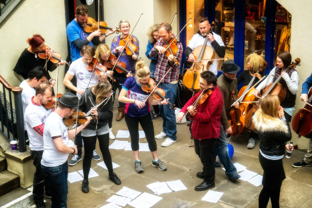 Eine Gruppe von Menschen, die Geigen spielen mit verstreuten Papieren auf dem Boden.